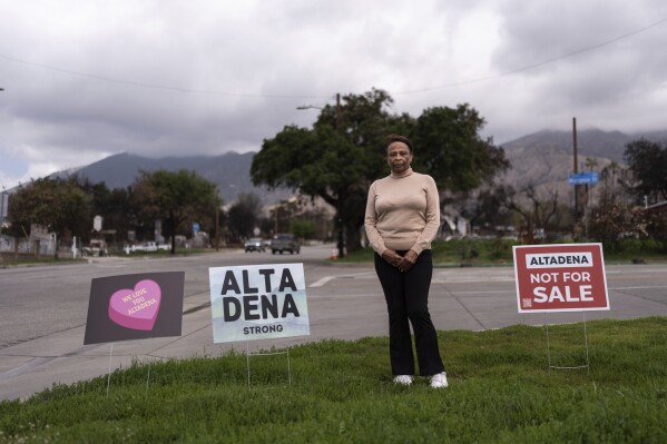 Barbara Shay, the owner of the Little Red Hen cafe, which was destroyed in the Eaton fire, represents a portrait next to signs in Altadena, California, Friday, March 28, 2025 (AP Photo/Jae C. Hong)